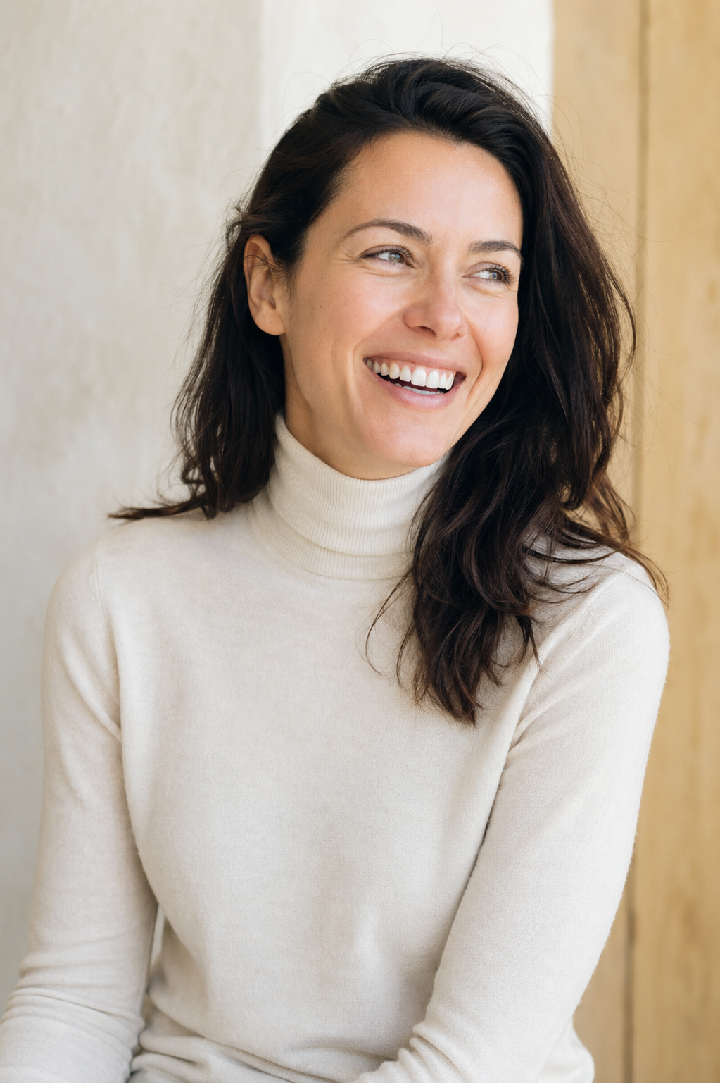 Portrait of a smiling woman with dark hair in a white turtleneck, warm natural light